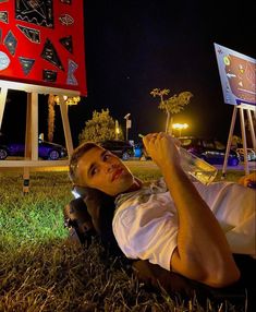 a man laying on the ground in front of some signs at night with his hand up to his face