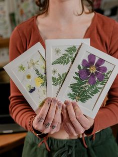 a woman holding four cards with flowers on them