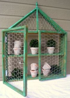 a green shelf with potted plants in it on the side of a house made out of chicken wire