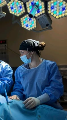 two doctors in scrubs and masks operating on a patient's head with lights above them