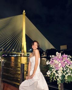 a woman in a white dress is posing for a photo by the water at night