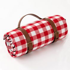 a red and white checkered picnic blanket with brown leather straps on the handle is shown