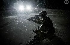 a soldier sitting on the ground in the dark with a flashlight shining through his eyes