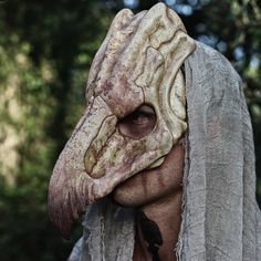 a man wearing an alien mask with trees in the background