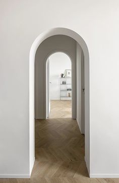 an arch leading into a white room with wood floors