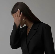 a woman in a black suit holding her hand up to her face