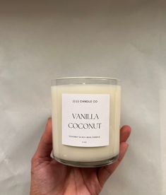 a hand holding a candle that says vanilla coconut on the front and side of it