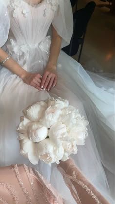 a woman in a wedding dress sitting on a chair with her bouquet and bride's shoes