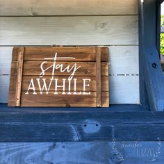 a wooden sign that says stay awhile on the side of a blue building with white lettering