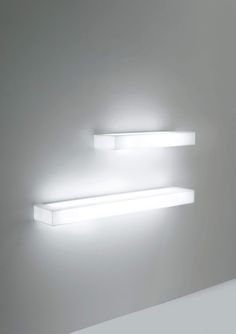 two white shelves with lights on them against a wall in a dimly lit room that appears to be empty