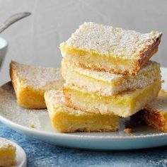 four pieces of lemon bars on a plate with a cup of coffee in the background