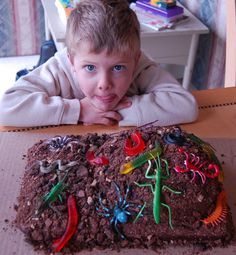 a young boy sitting at a table in front of a cake with bugs on it