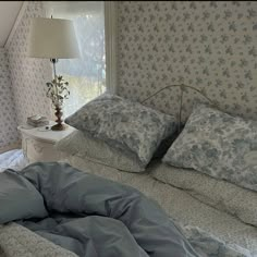 a bed sitting under a window next to a nightstand with a lamp on top of it