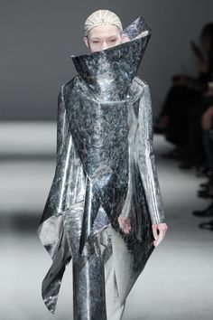 a woman in a silver outfit walking down a runway with an umbrella over her head