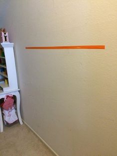 the corner of a room with an orange line on the wall next to a white shelf