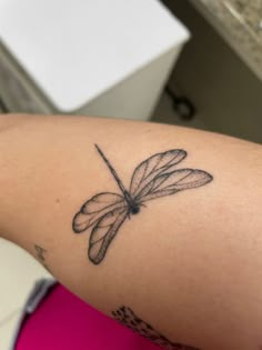 a woman's arm with a dragonfly tattoo on the back of her left arm