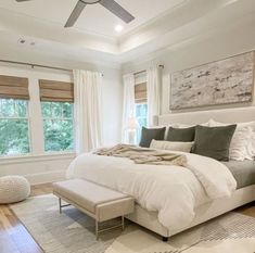 a large white bed sitting in a bedroom next to two windows and a rug on the floor