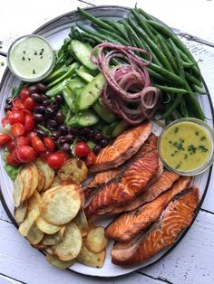 a white plate topped with fish, veggies and tomatoes next to green beans