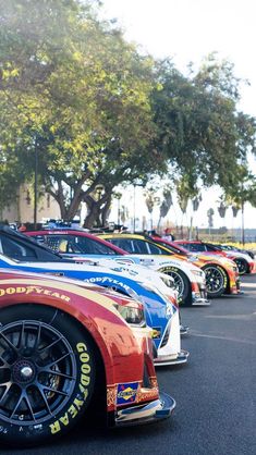 a row of cars parked next to each other in a parking lot with trees behind them