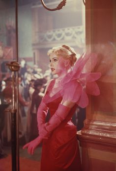 a woman in a red dress standing next to a clock with people looking on from behind it