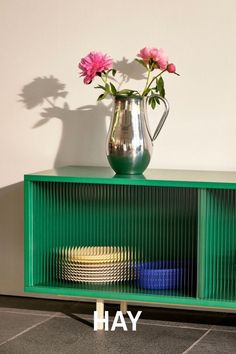 a vase with flowers on top of a green sideboard next to plates and cups