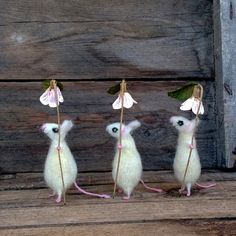 three little mouses with flowers in their ears on a wooden table next to a wall