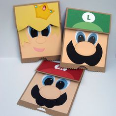 three boxes with paper cut out of them on top of a white table and one has an image of mario