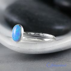 This Sterling Silver Blue Opal Ring features an 8 mm x 6 mm oval lab grown Blue Opal cabochon that has been securely set in a highly polished fine silver bezel. The band is made of a sturdy round Sterling Silver wire that has a hammered texture around the entire band. These beautiful rings make unique promise rings, lovely stacking rings, great birthstone rings, or just a wonderful love tokens for yourself or your special someone. This man-made Blue Opal is created from very uniform nanoparticle Modern Oval Cabochon Opal Ring As Gift, Classic Blue Oval Opal Ring, Classic Blue Opal Ring As A Gift, Classic Blue Opal Ring As Gift, Classic Oval Blue Moonstone Ring, Classic Blue Opal Ring For Gift, Classic Blue Opal Ring Gift, Blue Cabochon Opal Ring, Blue Cabochon Opal Ring For Anniversary