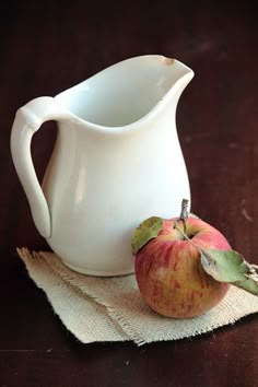 an apple sitting on top of a cloth next to a white pitcher