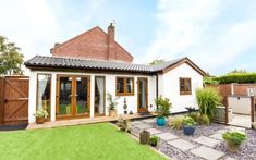 a small white house sitting on top of a lush green field next to a wooden fence