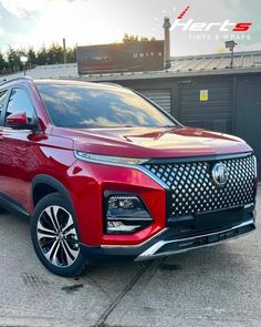 the front end of a red suv parked in a parking lot next to a building