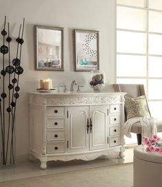 a white bathroom vanity sitting next to a chair in a room with two pictures on the wall