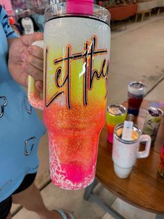 a person holding up a pink and yellow tumbler with the word let the beat on it