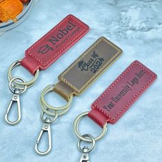 three leather keychains sitting on top of a white table next to oranges