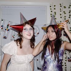 two young women wearing party hats in front of a wall with confetti on it