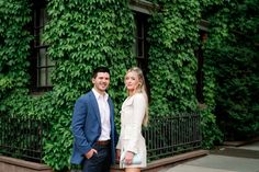 a man and woman standing next to each other in front of green ivy covered buildings