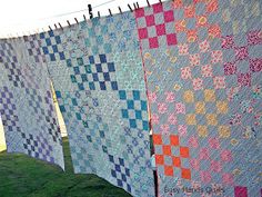 several quilts hanging on clothes line in the grass