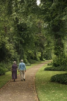 an older couple walking down a path in the park together, holding hands and looking at each other