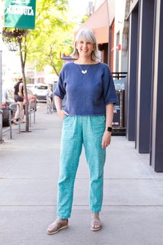 a woman standing on the sidewalk in front of a building with her hands in her pockets