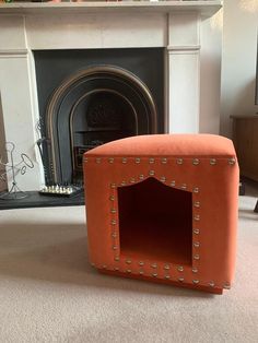 an orange ottoman sitting in front of a fire place with a dog house built into it