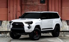 a white toyota suv parked in front of a red building with shutters on it