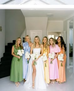 a group of women standing next to each other in front of a white wall holding bouquets