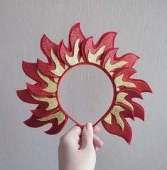 a hand holding up a red and gold heart shaped paper decoration with flames on it