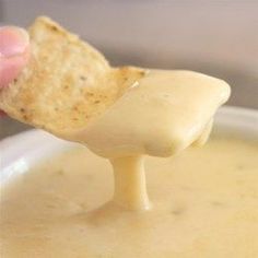 a cracker dipping cheese into a bowl of soup