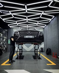 a man standing next to a black car in a garage with lights hanging from the ceiling