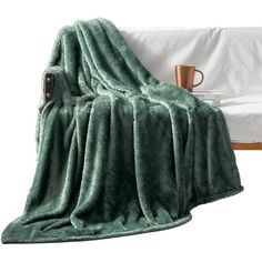 a green blanket sitting on top of a bed next to a cup