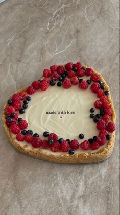 a heart shaped cake with berries and cream on it that says made with love in the center