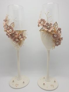 two wine glasses decorated with flowers and gold trimmings, one is white the other is pink