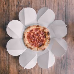 a pizza sitting inside of a paper flower on top of a wooden table