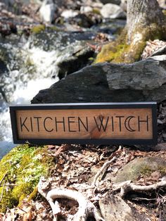 a sign that reads kitchen witch next to some rocks and water in the stream behind it